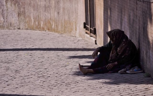 An old woman sitting alone on a cobblestone street