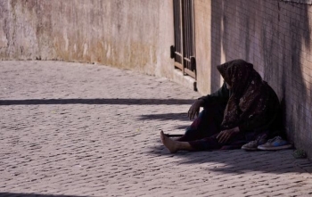 An old woman sitting alone on a cobblestone street
