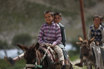 Two Afghani displaced children riding horses.