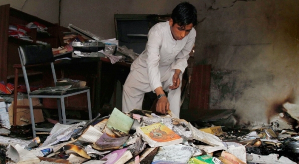 Un bambino afghano raccoglie dei libri tra le macerie di una scuola nella provincia di Nangarhar, Kabul