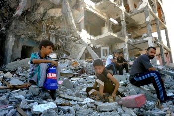 Palestinesi seduti tra le macerie