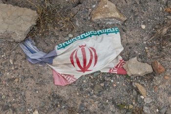  Iranian flag laying on the ground next to rocks.
