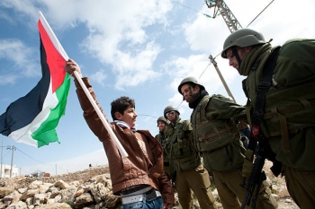 Un giovane sventola la bandiera Palestinese davanti a soldati Israeliani
