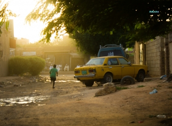 Young boy running in an almost desert Khartoum with a yellow taxi nearby