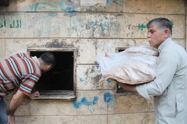 Two men are in front of a building in Aleppo, collecting daily bread relief  