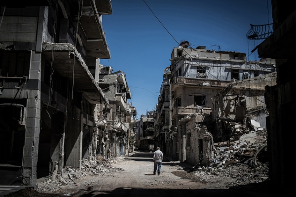 Un rifugiato siriano a Homs, in Siria, cammina lungo una strada devastata da armi esplosive a giugno 2014.