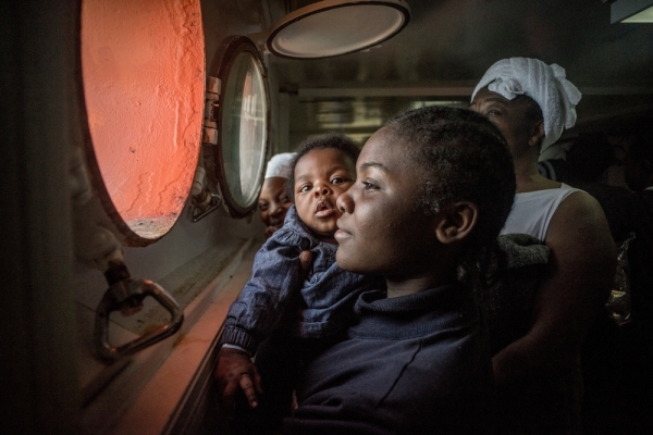 &ldquo;Search and Rescue&rdquo; - A young African woman holding her baby tries to catch sight of European shores through the porthole.  