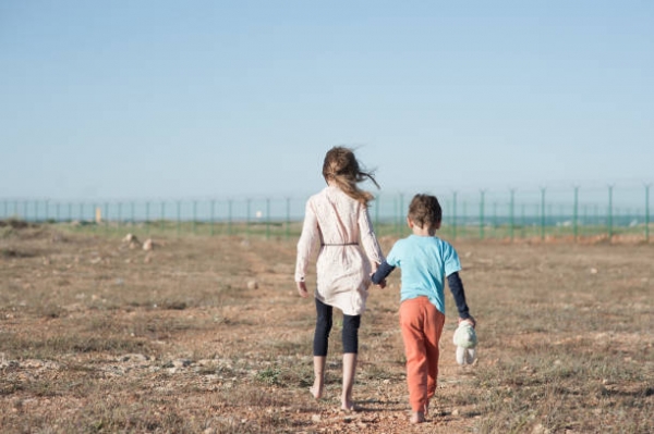 Un bambino ed una bambina camminano scalzi sul terreno sterrato.