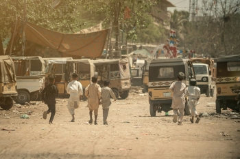 Children running in a dusty street near vehicles