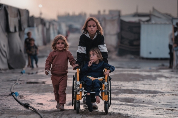 Tre bambine, una in sedia a rotelle, avanzano tra le macerie di Gaza