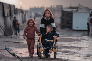 Tre bambine, una in sedia a rotelle, avanzano tra le macerie di Gaza