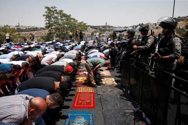 Palestinesi in preghiera attorno ai cancelli di al-Aqsa, di fronte ai poliziotti israeliani che vietano l&rsquo;ingresso.