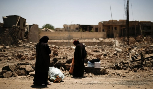 In fuga da Mosul, due donne irachene sostano per occuparsi del proprio bagaglio.  