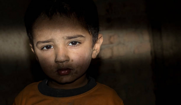  Un bambino rifugiato senza tetto in piedi in una stanza buia con un&#039;espressione triste. 