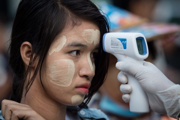 A Myanmar woman wearing a traditional facial cosmetic is being checked for fever 