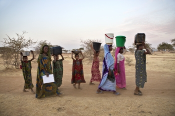 Malian refugee women carry water to their shelters in a nearby camp 
