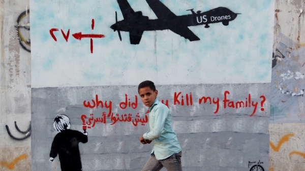 Un ragazzo yemenita vicino a un graffito raffigurante un drone americano e la scritta “perché hai ucciso la mia famiglia?”