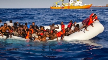 Richiedenti asilo chiedono aiuto dal gommone che imbarca acqua mentre sullo sfondo la nave Aquarius arriva in soccorso.