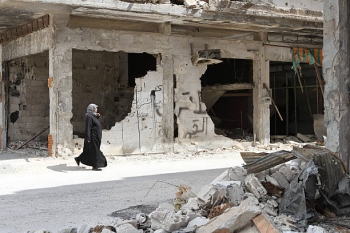 A woman walks near a house in the city of Homs 