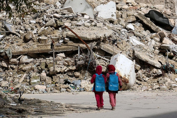 Two  girls in Aleppo walk home from school alongside a mound of rubble