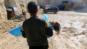 Un uomo porta il corpo di un bimbo deceduto a causa di un attacco chimico in Siria 
