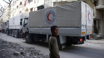 Un bambino siriano guarda il passaggio dei furgoni della Croce Rossa trasportare aiuti umanitari a Douma.