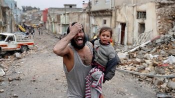 Un uomo disperato, con una bambina tra le braccia, cammina tra le macerie della città vecchia di Mosul
