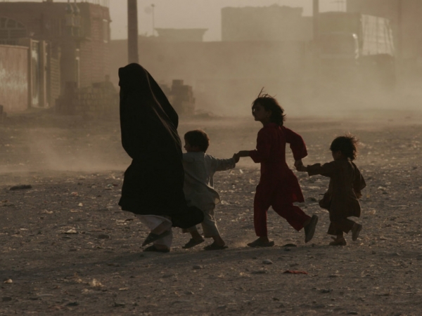 Una donna con i suoi bambini mentre corrono in una strada polverosa di Herat, Afghanistan