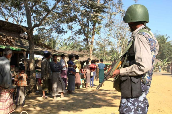 Myanmar border guard standing near a group of Rohinhya Muslims  