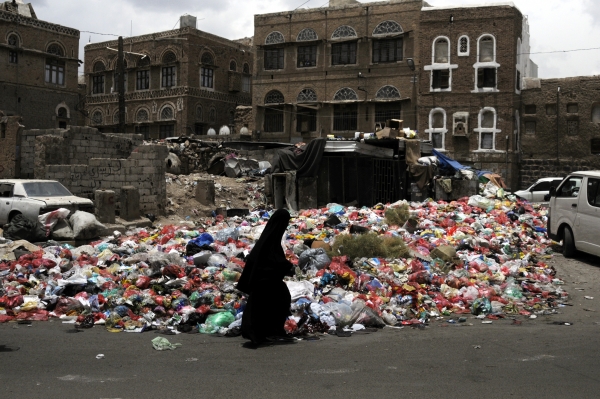 A woman walking next to rubbish heaps on the streets of Sana’a