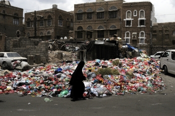Una donna cammina vicino a cumuli di spazzatura nelle strade di Sana’a