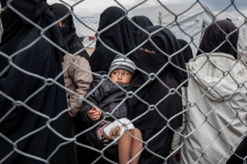 Una donna trasporta un bambino ferito in mezzo ad un gruppo di donne in un campo siriano 