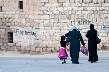 Two Palestinian women and a girl walk down a city street in the city of Hebron.