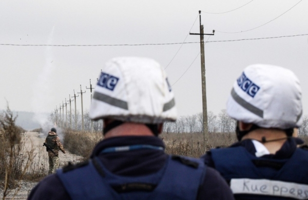 OSCE observers stand behind an officer launching signal rockets near Bohdanivka, in Donetsk region, 2019