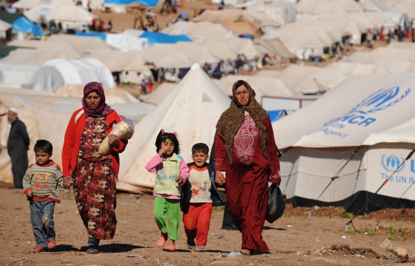 Two women walk alongside their children in a Syrian refugee camp