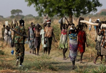 Women carrying their belongings in northern South Sudan are passed by a soldier