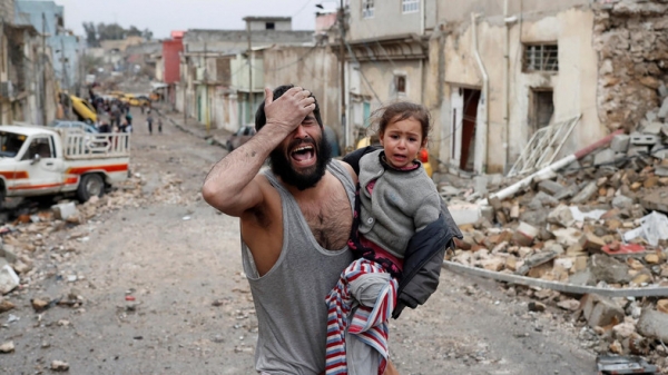 A desperate man with a young girl in his arms, walking amongst the ruins of the Old City of Mosul.