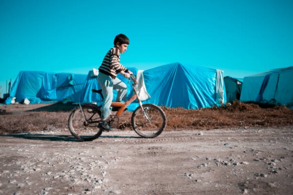 Bambino siriano in sella a una bici in un campo profughi